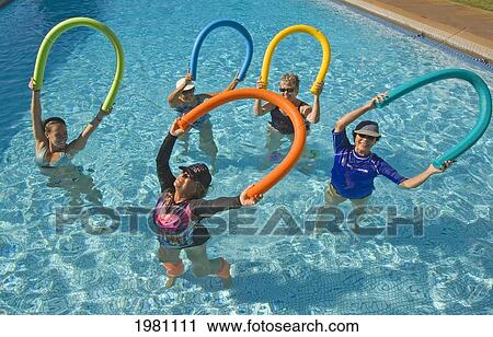 Stock Image - Hawaii, Maui, Paia, Maui Country Club, Aquasize Class, Smiling Women Demonstrating Move With Colorful Devices.. Fotosearch