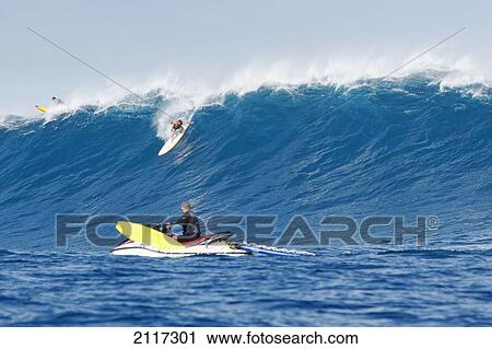 Stock Image - Hawaii, Maui, Peahi, Surfer rides a giant wave at Peahi also know as Jaws with lifeguards ready for safety. EDITORIAL USE ONLY.. Fotosearch