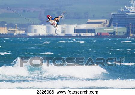 Stock Photograph - Hawaii, Maui, Professional Kiteboarder Niccolo Porcella Catching Air Off The North Shore, Buildings In Background. Editorial Use Only.. Fotosearch