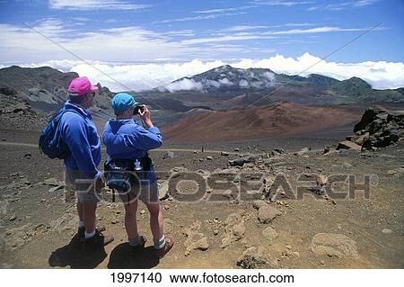 Stock Image - Hawaii, Maui, View From Behind Couple Hiking In Haleakala Crater National Park Taking Pictures A48D. Fotosearch