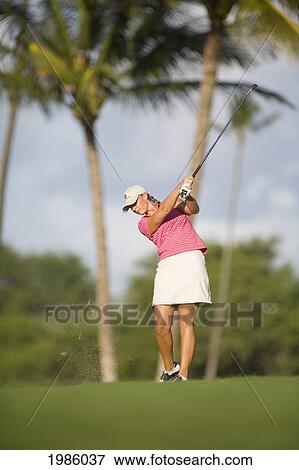 Stock Photo - Hawaii, Maui, Wailea Gold Golf Course, Female Golfer Swinging Golf Club, Turf Flying From Club, View From Front.. Fotosearch