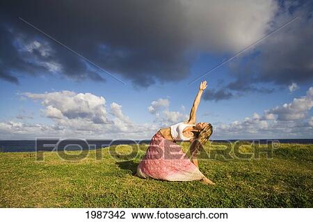 Stock Image - Hawaii, Maui, Young Woman Doing Yoga On Grassy Hill Next To The Ocean.. Fotosearch
