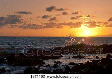 Stock Image - Hawaii, Molokai, Kaupoa Beach, Wave Splashing Onto A Rocky Shoreline At Sunset.. Fotosearch