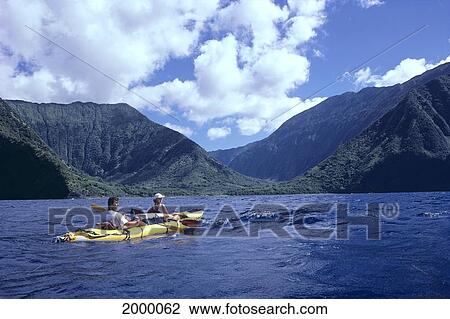 Stock Image - Hawaii, Molokai, North Coast, Couple Kayaking, Mountains And Coastline Background. Fotosearch