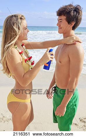 Stock Image - Hawaii, Oahu, A young couple help eachother apply sunscreen.. Fotosearch