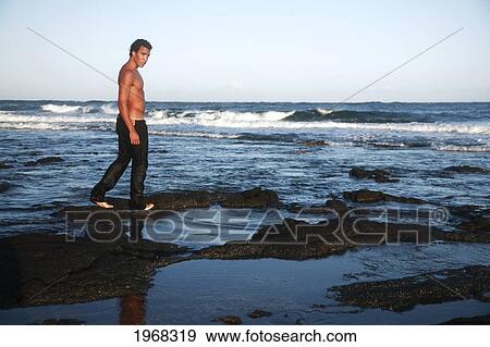 Hawaii, Oahu, Attractive Male Walking Along The Black Shoreline Rocks. View Large Photo Image Stock Photo - Hawaii, Oahu, Attractive Male Walking Along The Black Shoreline Rocks.. Fotosearch