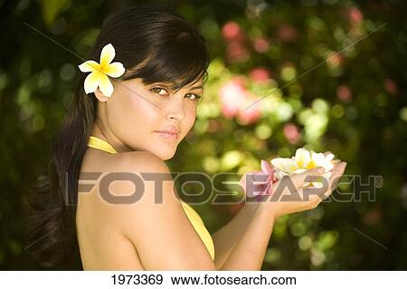 Stock Photo - Hawaii, Oahu, Beautiful Headshot Of A Young Girl With A Plumeria In Her Ear, Holding Plumerias In Her Hand.. Fotosearch