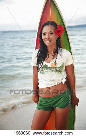 Stock Image - Hawaii, Oahu, Beautiful Local Girl Smiling And Holding A Colorful Surfboard At The Beach. Fotosearch