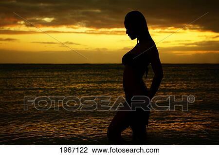 Stock Image - Hawaii, Oahu, Beautiful Silhouette Of Woman Standing In Ocean Water At Sunset.. Fotosearch