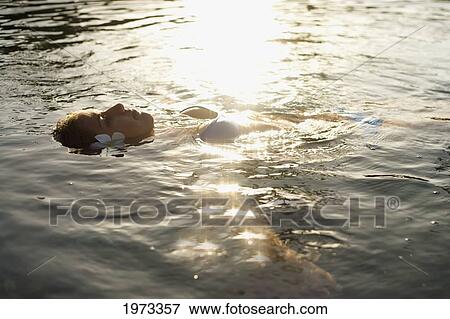 Hawaii, Oahu, Beautiful Woman Floating In The Water As The Sun Sets. View Large Photo Image Stock Photo - Hawaii, Oahu, Beautiful Woman Floating In The Water As The Sun Sets.. Fotosearch