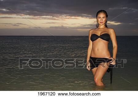 Stock Image - Hawaii, Oahu, Beautiful Woman Standing In Ocean Water At Sunset.. Fotosearch