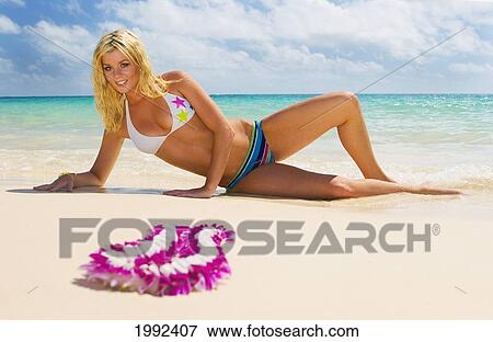Stock Photo - Hawaii, Oahu, Beautiful Young Woman Laying On A Tropical Beach, Lei In The Foreground.. Fotosearch
