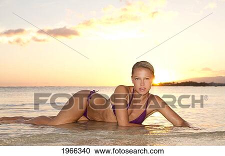 Stock Image - Hawaii, Oahu, Blond Woman Lounging In Shallow Ocean Water Along Seashore, Sunset Light.. Fotosearch