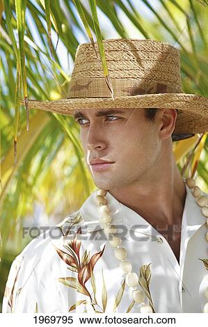 Stock Photography - Hawaii, Oahu, Closeup Headshot Of European Male Wearing Aloha Shirt With White Kukui Nut Lei And Rafia Hat, Palm Frond In The Background.. Fotosearch