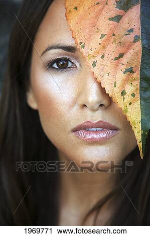 Stock Image - Hawaii, Oahu, Closeup Of Young Beauty Female Headshot With Colorful Leaves Next To Her Face.. Fotosearch