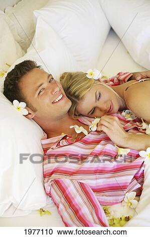 Stock Image - Hawaii, Oahu, Couple Cuddle In Hotel Bed Covered In Plumerias.. Fotosearch