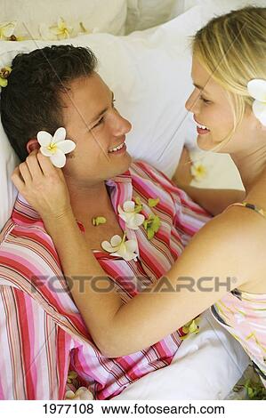 Stock Photo - Hawaii, Oahu, Couple Cuddle In Hotel Bed Covered In Plumerias.. Fotosearch