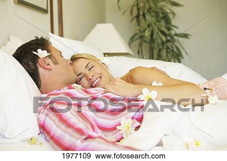 Stock Photo - Hawaii, Oahu, Couple Cuddle In Hotel Bed Covered In Plumerias.. Fotosearch