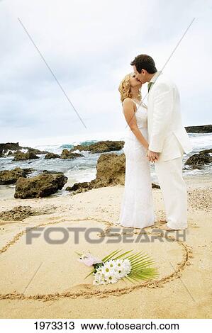 Hawaii, Oahu, Couple Holding And Kissing Each Other On The Shore With A Heart Shape Imprinted On The Sand In The Foreground With A Bouquet In It. View Large Photo Image Stock Image - Hawaii, Oahu, Couple Holding And Kissing Each Other On The Shore With A Heart Shape Imprinted On The Sand In The Foreground With A Bouquet In It.. Fotosearch