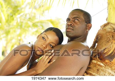 Stock Photo - Hawaii, Oahu, Couple Leaning On A Palm Tree In A Tropical Setting.. Fotosearch