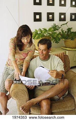 Stock Image - Hawaii, Oahu, Couple Looking Over Paper Work At Home.. Fotosearch