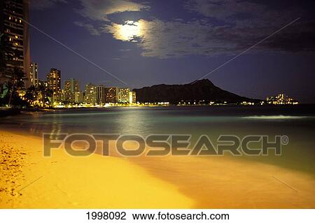 Stock Image - Hawaii, Oahu, Diamond Head At Night, Moon Hidden Behind Clouds, Bright Yellow Sand Skyline Illuminated. Fotosearch