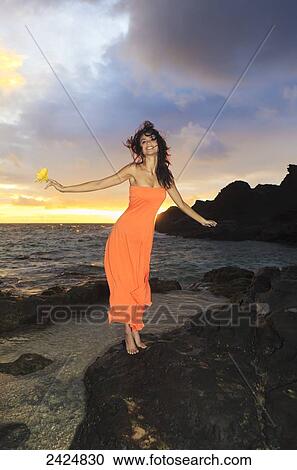 Hawaii, Oahu, Eternity Beach, Beautiful young woman in an orange dress holds a yellow hibiscus flower. View Large Photo Image Stock Image - Hawaii, Oahu, Eternity Beach, Beautiful young woman in an orange dress holds a yellow hibiscus flower.. Fotosearch