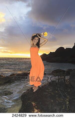 Hawaii, Oahu, Eternity Beach, Beautiful young woman in an orange dress holds a yellow hibiscus flower. View Large Photo Image Stock Photo - Hawaii, Oahu, Eternity Beach, Beautiful young woman in an orange dress holds a yellow hibiscus flower.. Fotosearch