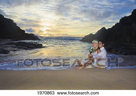 Stock Image - Hawaii, Oahu, Eternity Beach, Young Newlywed Couple Enjoy Sunrise On The Beach. Fotosearch