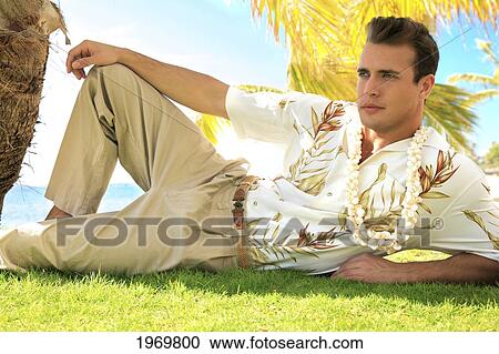 Stock Image - Hawaii, Oahu, European Male Leaning Against A Palm Tree And Relaxing At A Tropical Beach.. Fotosearch