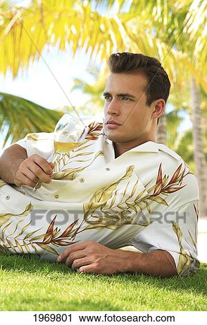 Stock Image - Hawaii, Oahu, European Male Leaning Against A Palm Tree And Relaxing At A Tropical Beach While Sipping Wine.. Fotosearch