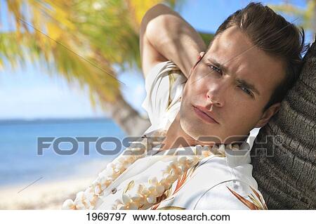 Stock Photo - Hawaii, Oahu, European Male Leaning Against A Palm Tree And Relaxing At A Tropical Beach.. Fotosearch