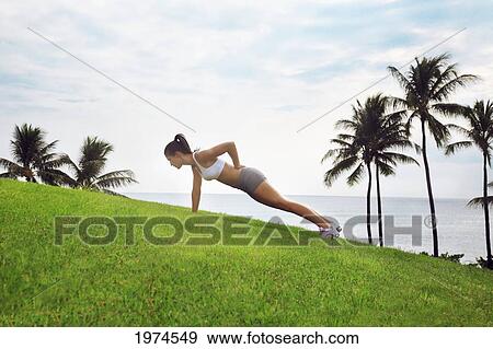 Stock Photo - Hawaii, Oahu, Female Doing One Hand Push Up On The Green Grass Next To Ocean And Palm Trees.. Fotosearch