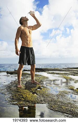 Stock Image - Hawaii, Oahu, Fit Male Drinking Water At The Tidepool.. Fotosearch