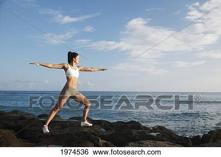 Stock Photograph - Hawaii, Oahu, Fit Young Girl On The Beach Doing Yoga On The Rocky Coastline.. Fotosearch