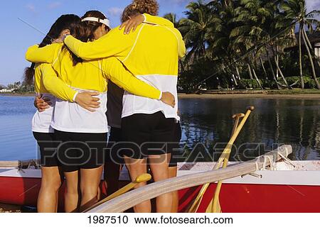 Stock Image - Hawaii, Oahu, Hawaii Kai, Women's Paddling Team Huddle On Beach Before Race, View From Behind. No Model Release. Fotosearch