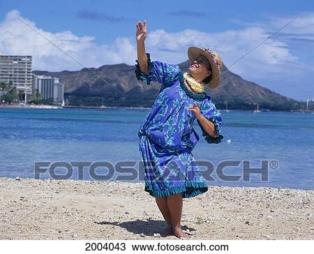Stock Image - Hawaii, Oahu, Hawaiian Woman Dances Hula On Beach Wearing Hat And Lei, Full Length View, Diamond Head Background. Fotosearch