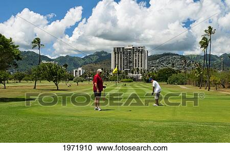 Stock Image - Hawaii, Oahu, Honolulu, Ala Wai Golf Course, A Local Golfer Watches His Friend Put On Hole Six.. Fotosearch