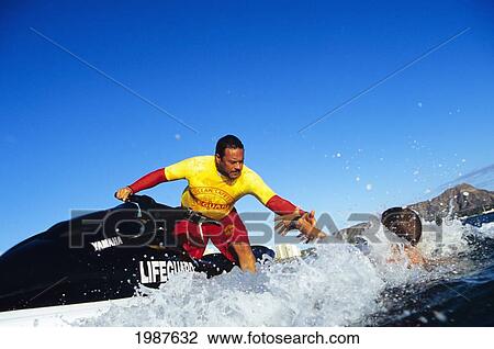 Stock Image - Hawaii, Oahu, Honolulu, Rescue Jet Ski, Lifeguard Demonstrating Safe Water Pickup. No Model Release. Fotosearch