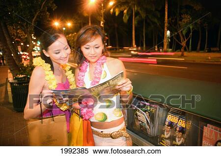 Hawaii, Oahu, Honolulu, Two Female Japanese Tourists Shopping In Waikiki At Night, Looking At A Free Brochure. View Large Photo Image Stock Photography - Hawaii, Oahu, Honolulu, Two Female Japanese Tourists Shopping In Waikiki At Night, Looking At A Free Brochure.. Fotosearch
