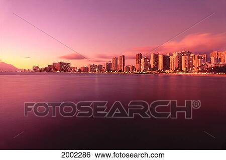 Stock Photograph - Hawaii, Oahu, Honolulu, Waikiki At Sunset, View From Across Ocean, Purple Pink Golden Hues Reflections On Water, Skies. Fotosearch