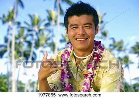 Stock Photography - Hawaii, Oahu, Japanese Man Wearing Lei Making Shaka Sign, Palm Trees In Background.. Fotosearch