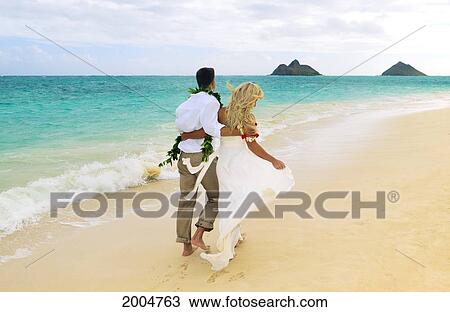 Stock Image - Hawaii, Oahu, Kailua, Lanikai Beach, Attractive Newlywed Couple Walking Along Beach, View From Behind.. Fotosearch
