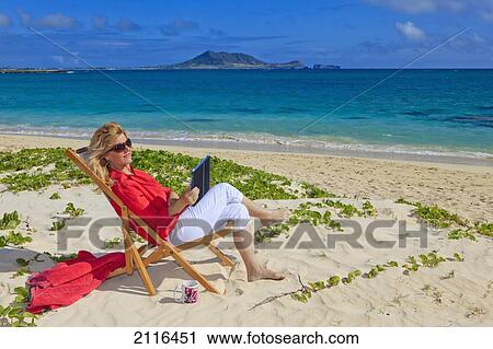 Stock Image - Hawaii, Oahu, Kailua, Lanikai Beach, Woman on beach uses electronic tablet.. Fotosearch