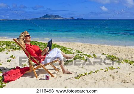 Stock Image - Hawaii, Oahu, Kailua, Lanikai Beach, Woman on beach uses electronic tablet.. Fotosearch