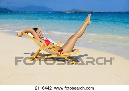 Stock Image - Hawaii, Oahu, Kailua, Lanikai, Beautiful woman stretches in a lounge chair on the beach.. Fotosearch