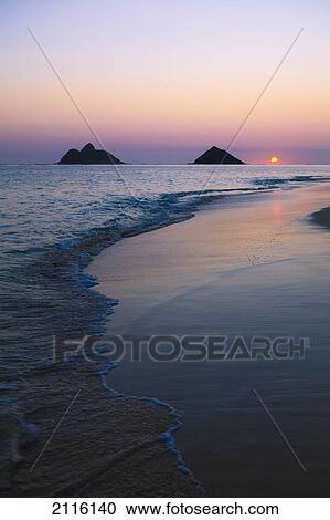 Stock Image - Hawaii, Oahu, Kailua, Lanikai, Sun sinking below horizon on beach.. Fotosearch