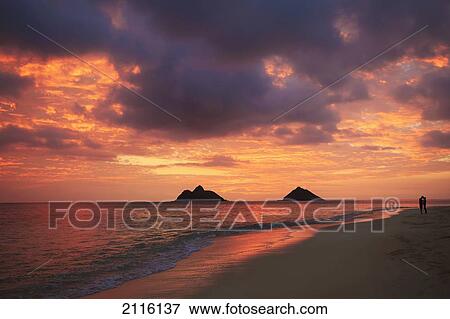 Stock Photo - Hawaii, Oahu, Kailua, Lanikai, Vibrant sunset with a couple embracing on beach.. Fotosearch