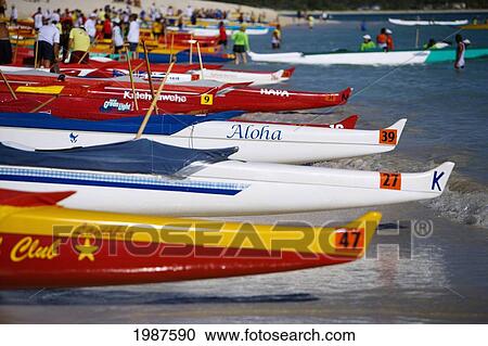 Stock Image - Hawaii, Oahu, Kailua, Lineup Of Colorful Outrigger Canoes On The Shoreline At A Canoe Race. Fotosearch