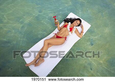 Stock Image - Hawaii, Oahu, Kaneohe Bay, Woman Floating On A Raft With A Tropical Drink. Fotosearch